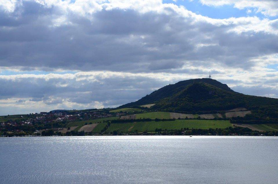 Výhled přes vodní hladinu na zalesněný kopec s vinicemi
